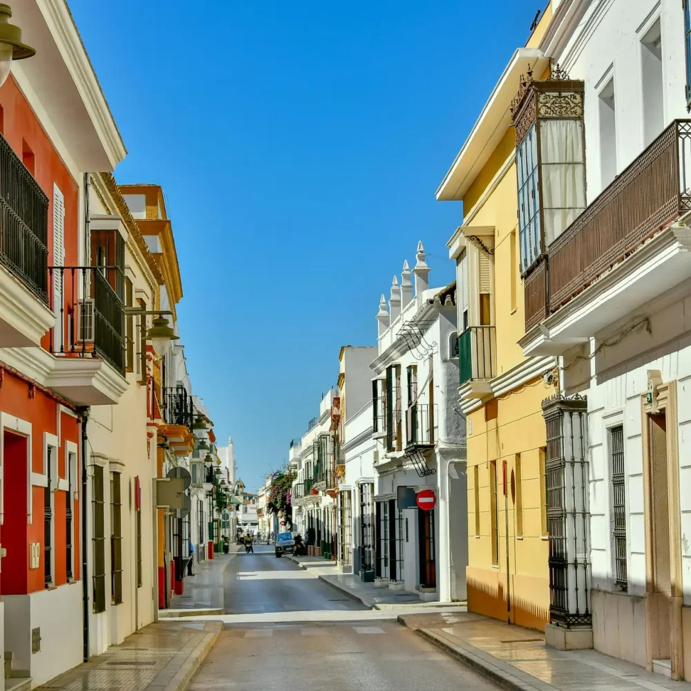 Charming street scene in Chipiona, Spain featuring colorful residential buildings and clear blue skies.